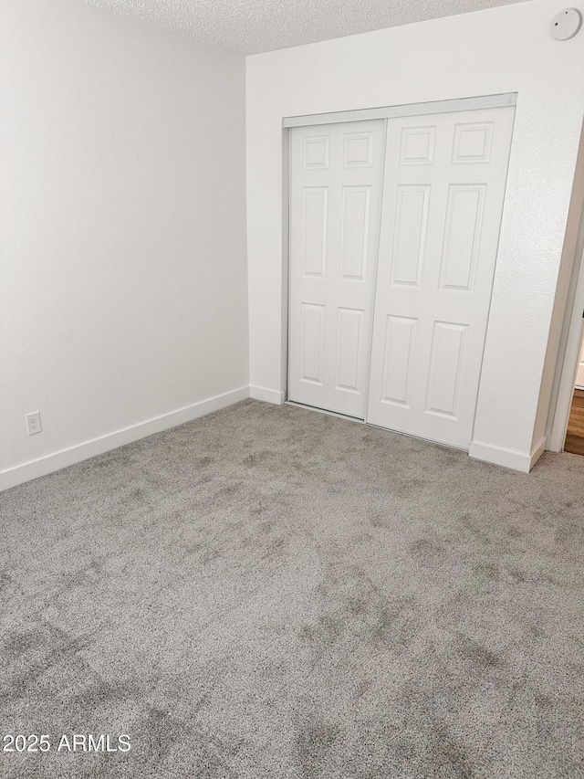 unfurnished bedroom featuring carpet floors, a closet, a textured ceiling, and baseboards