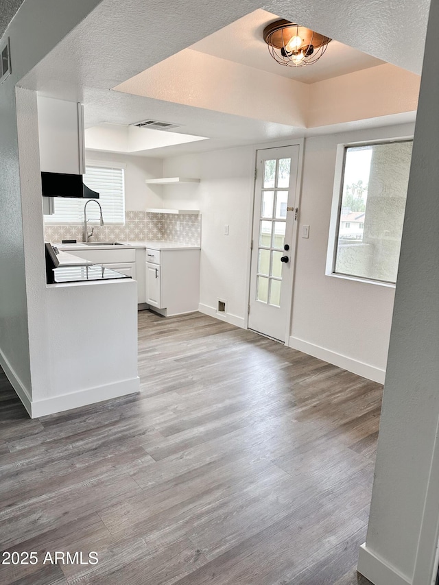 kitchen featuring a textured ceiling, a sink, white cabinetry, light wood-type flooring, and backsplash