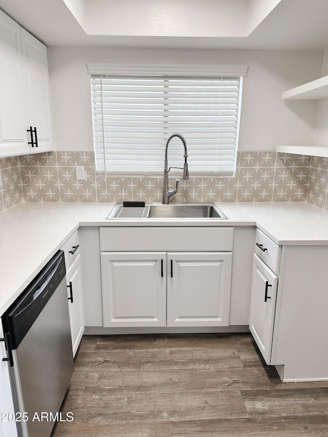 kitchen featuring wood finished floors, a sink, white cabinets, stainless steel dishwasher, and backsplash