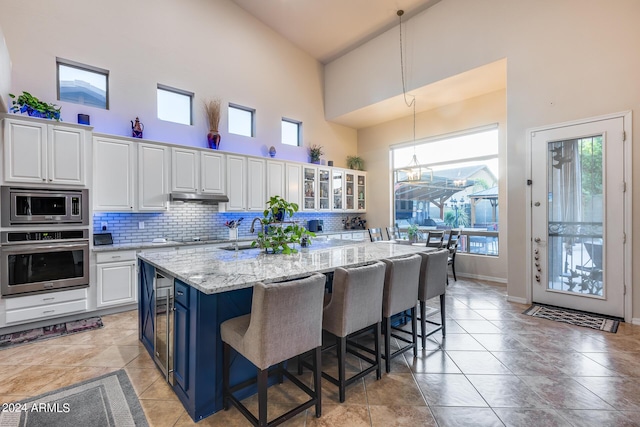 2728 W Adventure Dr, Anthem, AZ 85086 - kitchen with stainless steel appliances, high vaulted ceiling, white cabinets, blue cabinets, and under cabinet range hood