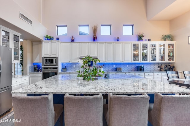 2728 W Adventure Dr, Anthem, AZ 85086 - kitchen featuring appliances with stainless steel finishes, a center island, a breakfast bar, white cabinetry, and a high ceiling