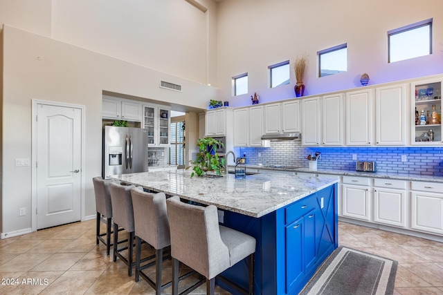2728 W Adventure Dr, Anthem, AZ 85086 - kitchen featuring a high ceiling, stainless steel refrigerator with ice dispenser, decorative backsplash, a breakfast bar, and glass insert cabinets
