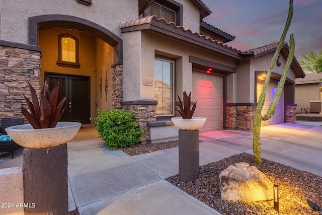 2728 W Adventure Dr, Anthem, AZ 85086 - exterior entry at dusk featuring stone siding, stucco siding, driveway, a tile roof, and an attached garage