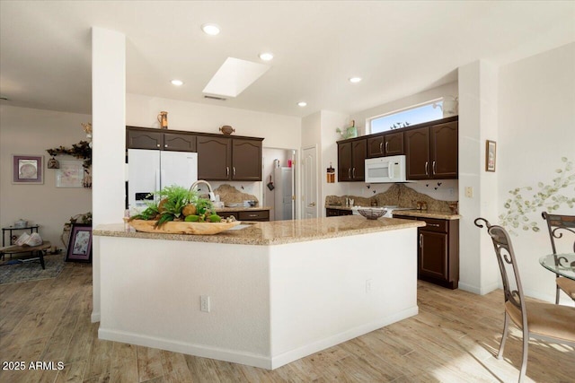 kitchen with light hardwood / wood-style floors, dark brown cabinets, white appliances, and a skylight