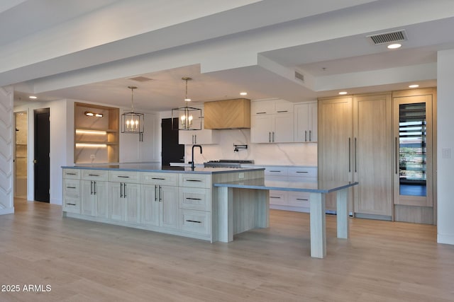 kitchen featuring a notable chandelier, tasteful backsplash, visible vents, light wood-style floors, and a sink