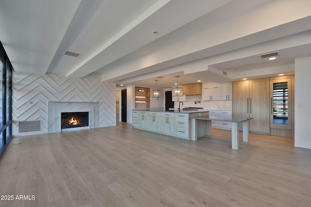 unfurnished living room with a high end fireplace, visible vents, a sink, and light wood-style flooring