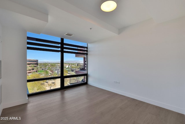 spare room featuring baseboards, wood finished floors, visible vents, and floor to ceiling windows