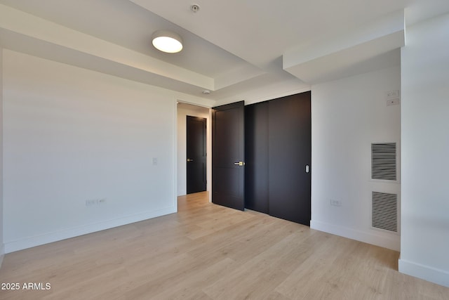 unfurnished bedroom featuring baseboards, a tray ceiling, and light wood-style floors