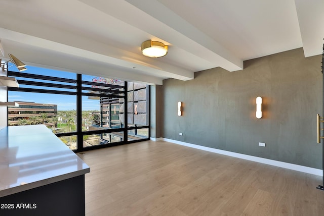 spare room featuring expansive windows, beamed ceiling, baseboards, and wood finished floors