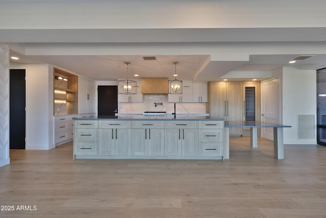 kitchen with light wood-type flooring, visible vents, a large island with sink, and decorative backsplash