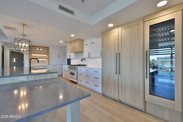 kitchen with premium range hood, a sink, visible vents, light wood-style floors, and high end stainless steel range