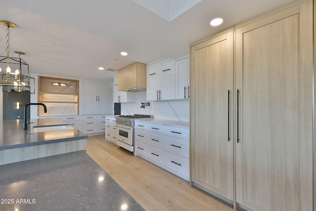 kitchen with high end stainless steel range, tasteful backsplash, recessed lighting, light wood-style flooring, and a sink