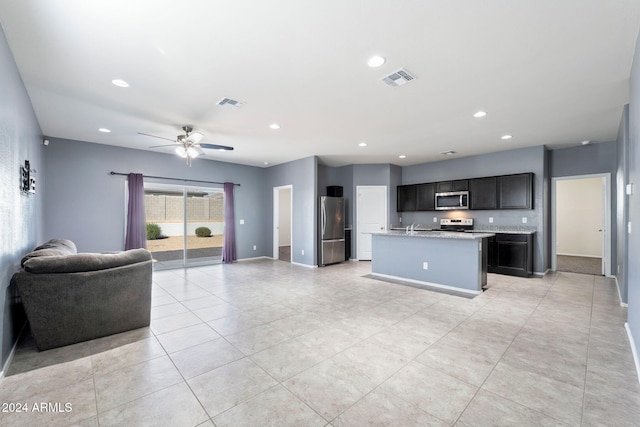 kitchen featuring light stone counters, a center island with sink, light tile patterned floors, appliances with stainless steel finishes, and ceiling fan