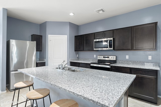 kitchen with sink, a kitchen bar, a kitchen island with sink, stainless steel appliances, and dark brown cabinets