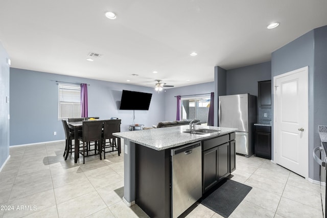 kitchen with appliances with stainless steel finishes, an island with sink, sink, light tile patterned floors, and light stone counters