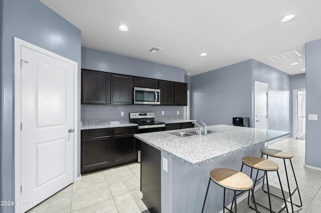 kitchen featuring appliances with stainless steel finishes, an island with sink, sink, a kitchen bar, and light stone countertops