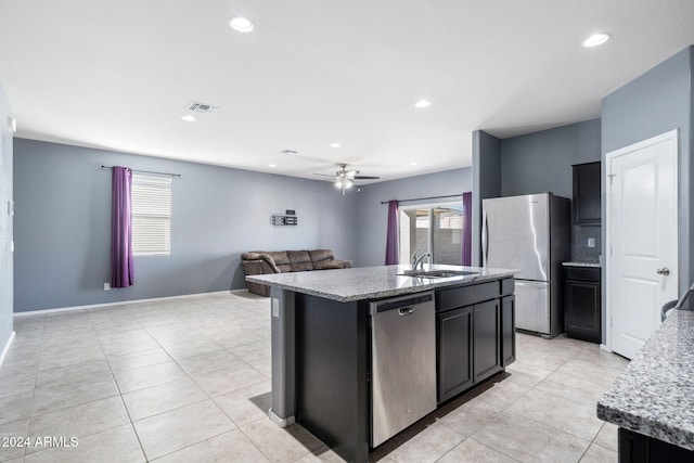 kitchen featuring sink, ceiling fan, appliances with stainless steel finishes, light stone countertops, and a center island with sink