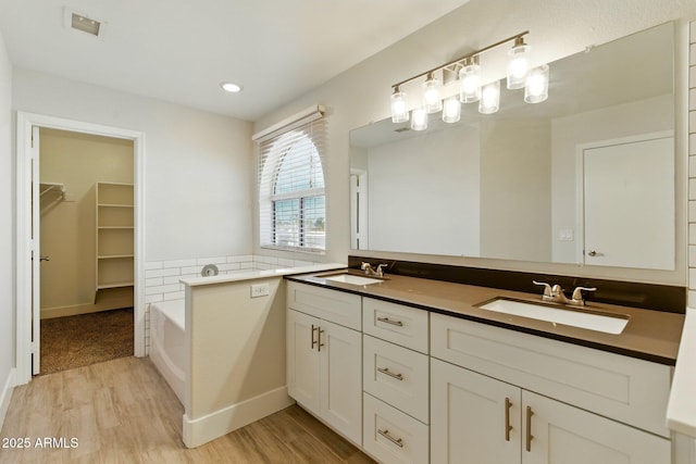 full bathroom with wood finished floors, a garden tub, a walk in closet, double vanity, and recessed lighting