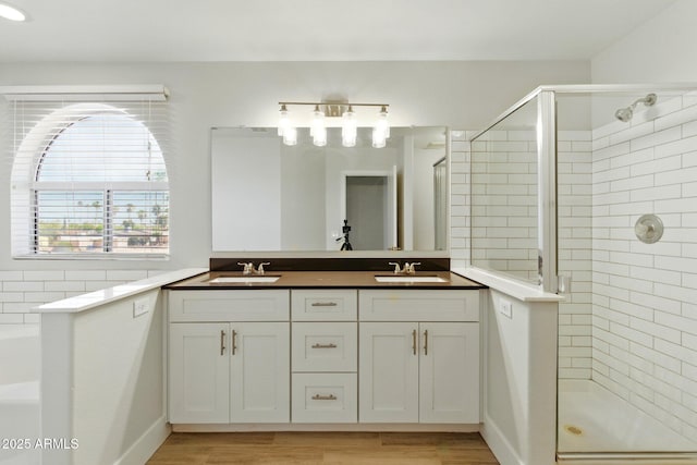 bathroom with a shower stall, double vanity, and wood finished floors