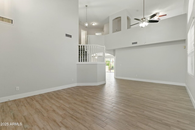 unfurnished living room featuring a towering ceiling, a ceiling fan, baseboards, and wood finished floors
