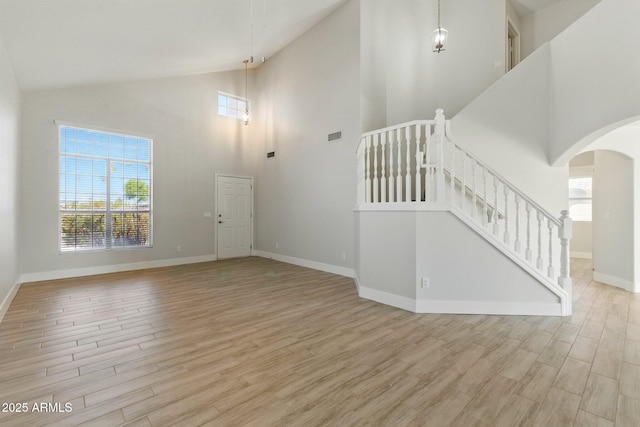 unfurnished living room with high vaulted ceiling, wood finished floors, plenty of natural light, and arched walkways
