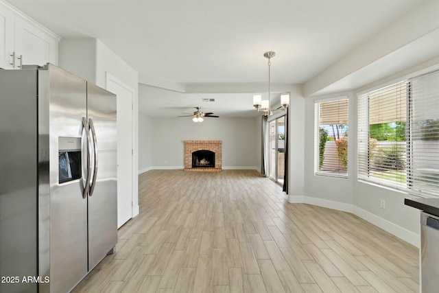 unfurnished living room featuring light wood finished floors, a brick fireplace, baseboards, and ceiling fan