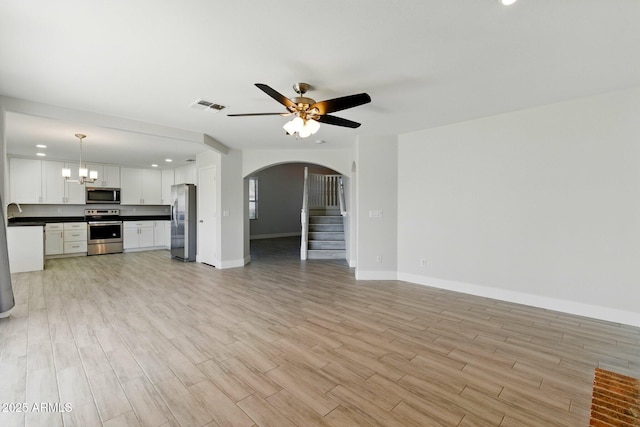 unfurnished living room with light wood-type flooring, arched walkways, baseboards, and ceiling fan