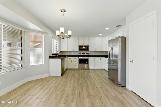 kitchen with appliances with stainless steel finishes, a chandelier, baseboards, dark countertops, and light wood-type flooring