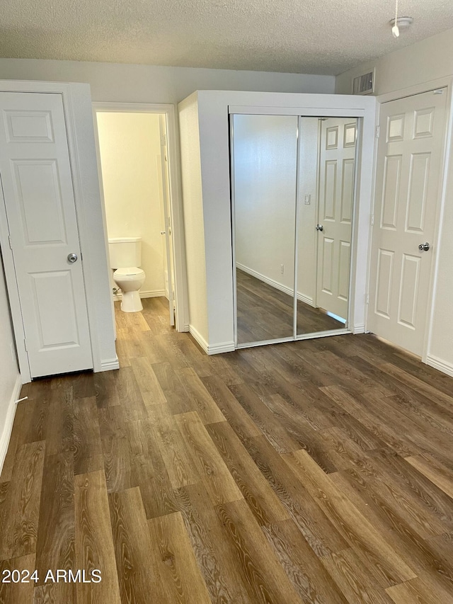 unfurnished bedroom featuring hardwood / wood-style flooring, ensuite bathroom, a textured ceiling, and a closet