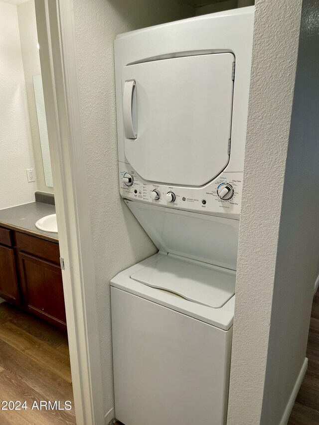 laundry area with sink, stacked washer and clothes dryer, and hardwood / wood-style flooring