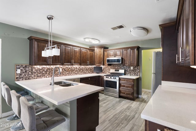 kitchen featuring sink, decorative backsplash, decorative light fixtures, kitchen peninsula, and stainless steel appliances