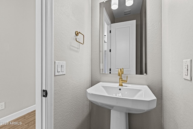 bathroom featuring a sink, a textured wall, baseboards, and wood finished floors