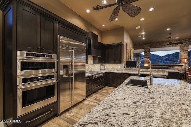 kitchen featuring backsplash, light stone counters, stainless steel appliances, ceiling fan, and light hardwood / wood-style floors