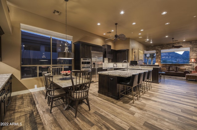 kitchen featuring light stone counters, a center island with sink, light hardwood / wood-style flooring, built in refrigerator, and hanging light fixtures