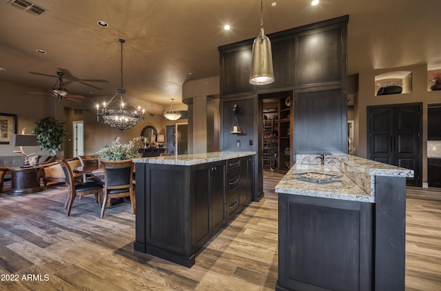 kitchen with ceiling fan with notable chandelier, a center island, light stone counters, and hanging light fixtures