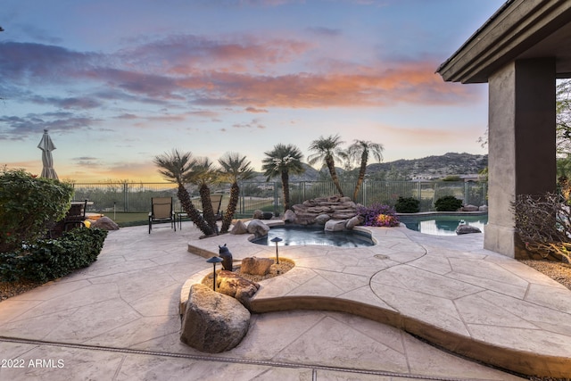 patio terrace at dusk featuring pool water feature, a mountain view, and a fenced in pool