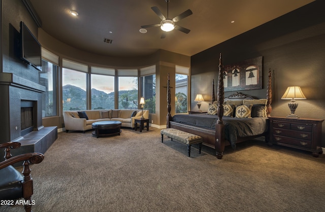 bedroom featuring a tile fireplace, carpet floors, and ceiling fan