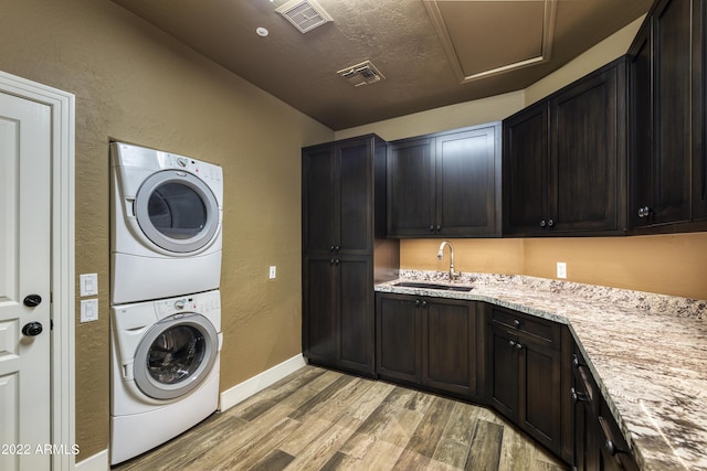 laundry area featuring stacked washer / drying machine, light hardwood / wood-style floors, cabinets, and sink