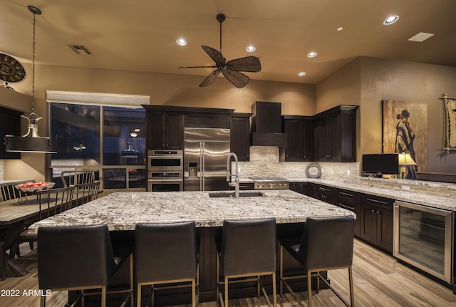 kitchen with a kitchen island with sink, sink, wine cooler, ceiling fan, and appliances with stainless steel finishes