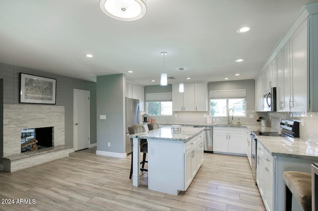 kitchen featuring a breakfast bar, a center island, white cabinetry, appliances with stainless steel finishes, and decorative light fixtures