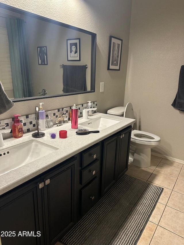 full bathroom with toilet, double vanity, a sink, and tile patterned floors