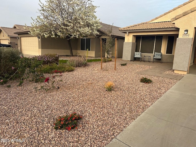 view of front of house featuring an attached garage, a patio area, a tile roof, and stucco siding