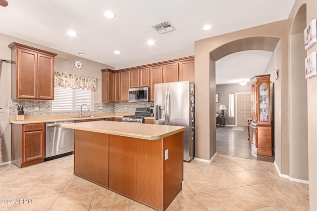 kitchen with decorative backsplash, appliances with stainless steel finishes, sink, a center island, and light tile patterned flooring