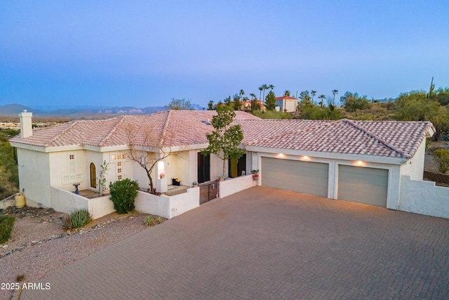 mediterranean / spanish house with a tiled roof, decorative driveway, an attached garage, and stucco siding