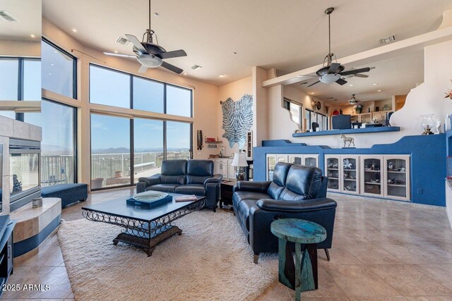 tiled living room with a ceiling fan, visible vents, and a high ceiling