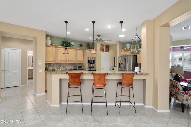 kitchen featuring light brown cabinetry, hanging light fixtures, a center island, stainless steel appliances, and light stone countertops