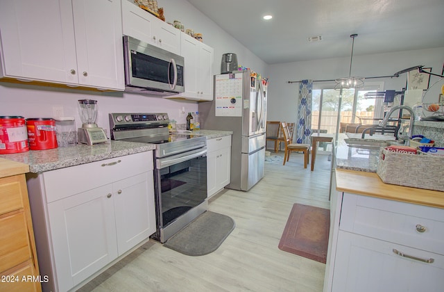 kitchen with white cabinets, hanging light fixtures, sink, light hardwood / wood-style flooring, and appliances with stainless steel finishes