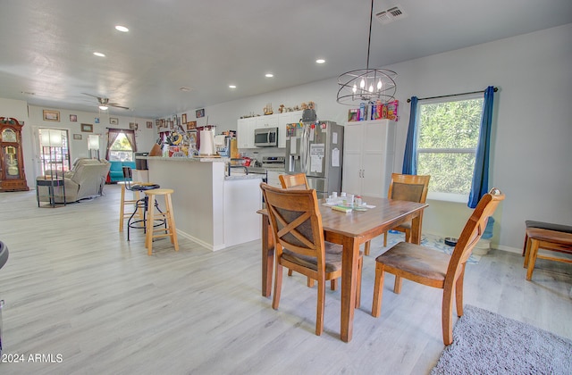 dining room with ceiling fan with notable chandelier and light hardwood / wood-style floors