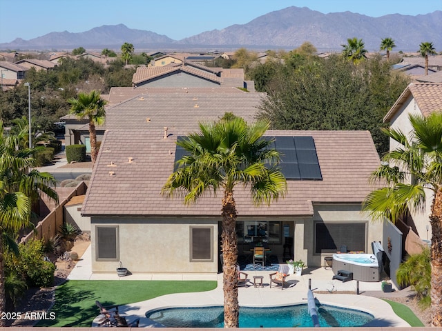 rear view of property featuring a patio, stucco siding, a hot tub, roof mounted solar panels, and a mountain view