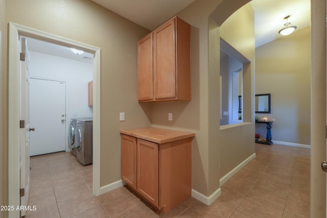 hallway with arched walkways, light tile patterned flooring, washing machine and clothes dryer, and baseboards